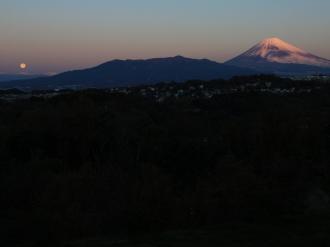暗い手前の山の向こうに富士山と上りはじめた満月が見える写真