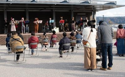 道の駅のステージ上で演奏する人たちとイスに座って聞き入る人たちの写真