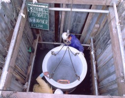 深い穴の底で丸い筒状のコンクリートブロックを設置している写真