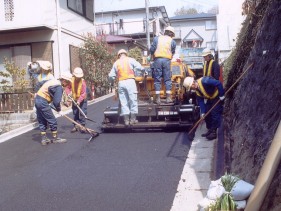 手作業と機械でアスファルトをならしている写真