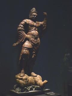 右手を腰にあて左手はこぶしを顔の高さまで上げて立っている毘沙門天立像の写真