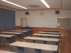 前にホワイトボードがあり数台の長机にそれぞれいすが3脚ずつ並べられている学習室の写真
