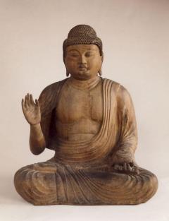 あぐらをかいて座り左手はひざに置き右手は胸のあたりの高さに上げ目をつぶっている薬師如来坐像の写真