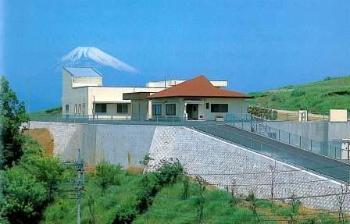 富士山を背景に丘の上にそびえる朱色の屋根の建物の写真