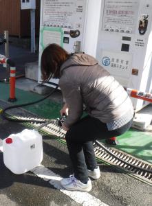白い自動販売機の前でダウンジャケットを着た後ろ姿の女性が給水を行っている写真