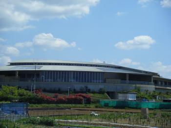 青空の下円形の屋根がついた青色の建物とその建物の周りに草木や畑がある写真