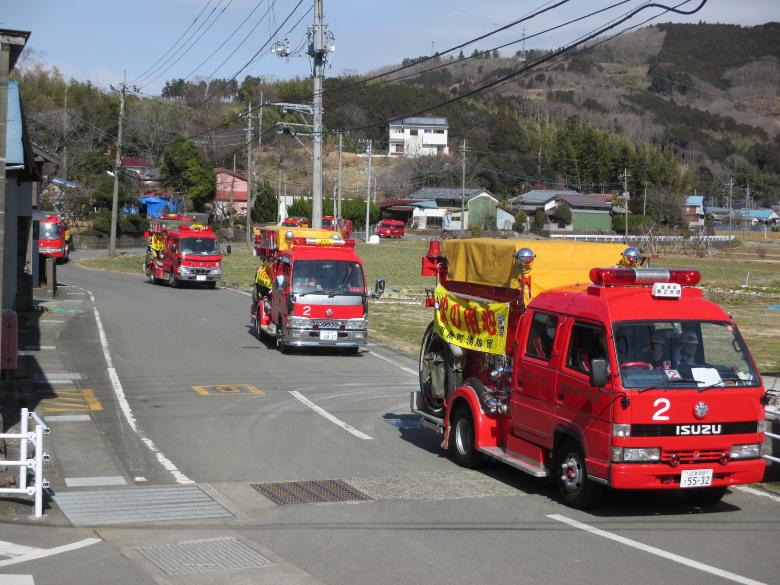 空き地と住宅の間をたくさんの消防車両が走っている防火パレードの写真