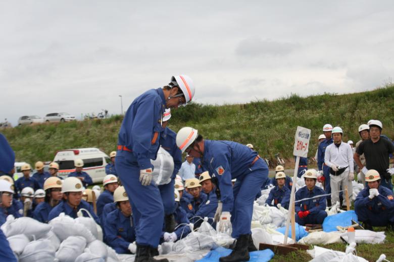 沢山の団員が見守る中土嚢を積んでいる隊員をとらえた水防訓練の写真